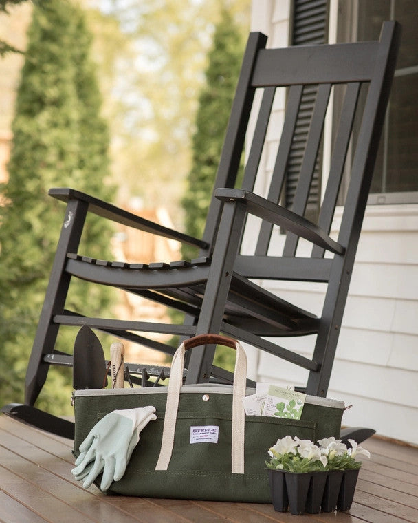 the garden tote loaded with tools resting on a porch alongside a rocking chair and pack of white flowers ready for planting