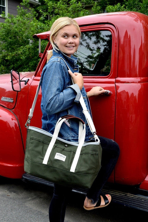 a model in a denim jacket with the garden tote slung over her shoulder with her hand on the door of a red truck