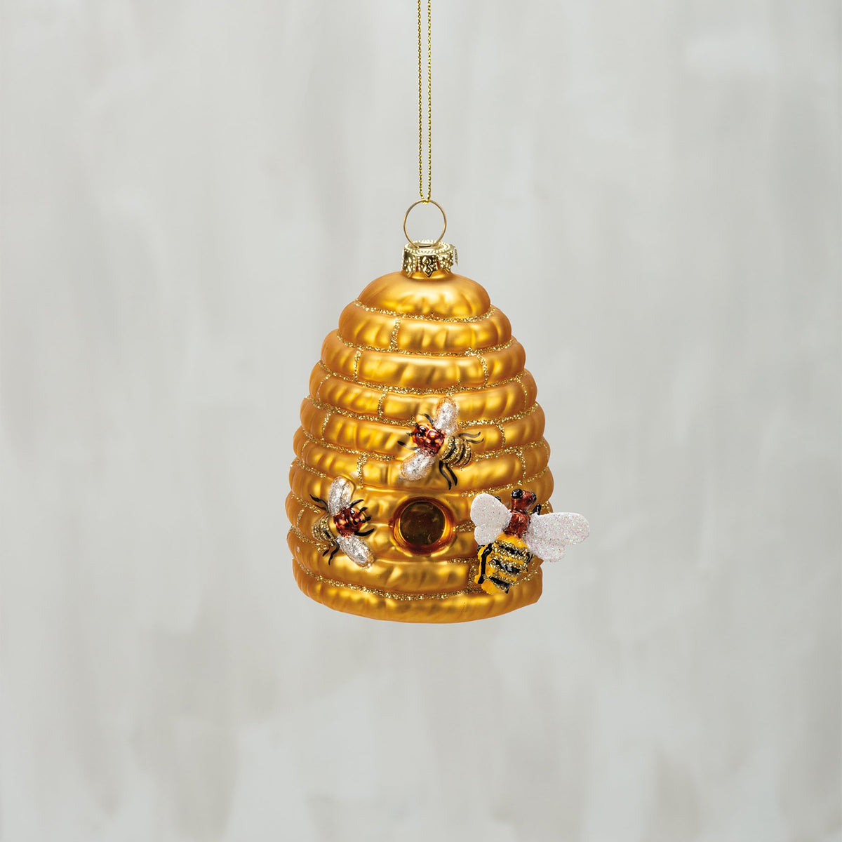 Decorative gold bee hive ornament with bees on a light gray background
