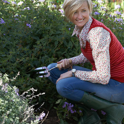 a gardener crouched in a lush garden holding the hand fork in her right hand