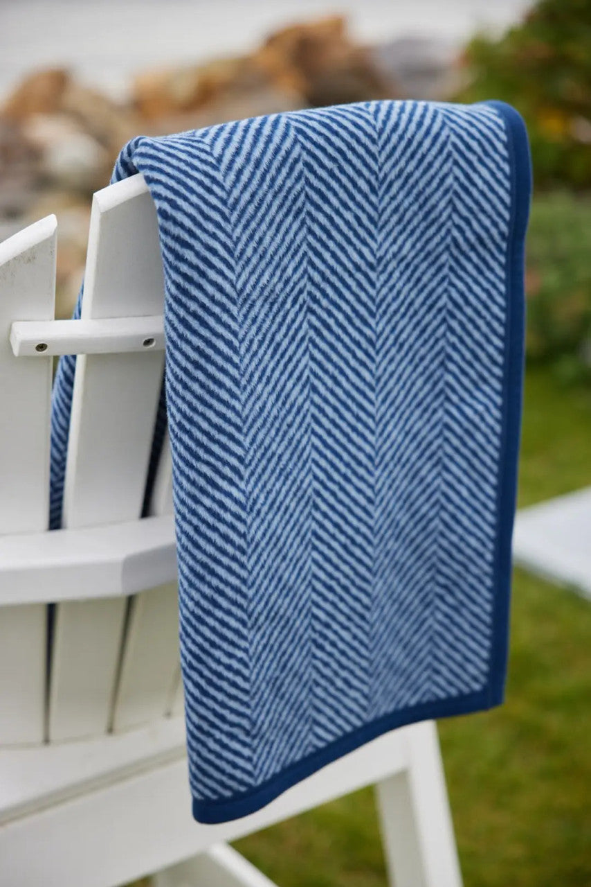 The folded Harborview Herringbone Navy Blanket draped over a white Adirondack chair
