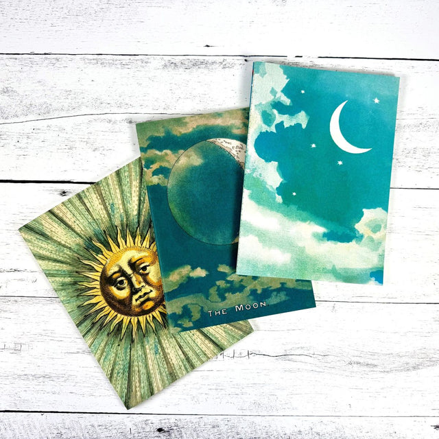 Three notebooks featuring celestial imagery on a wooden surface.