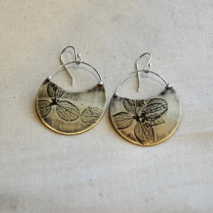 Pair of earrings with pressed hydrangea petal designs on a textured fabric background