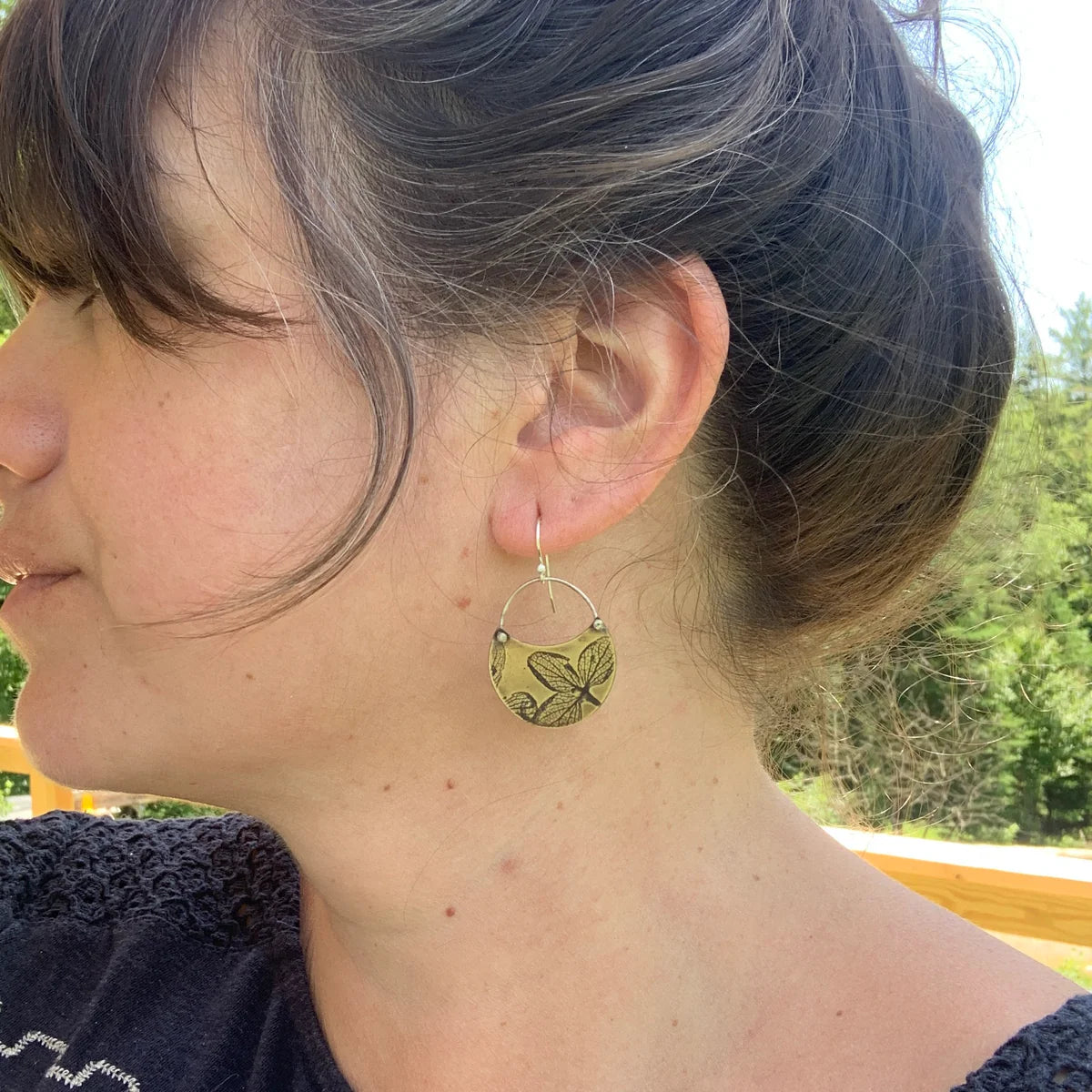 Close-up of a person wearing the hydrangea crescent earrings in brass with a natural background