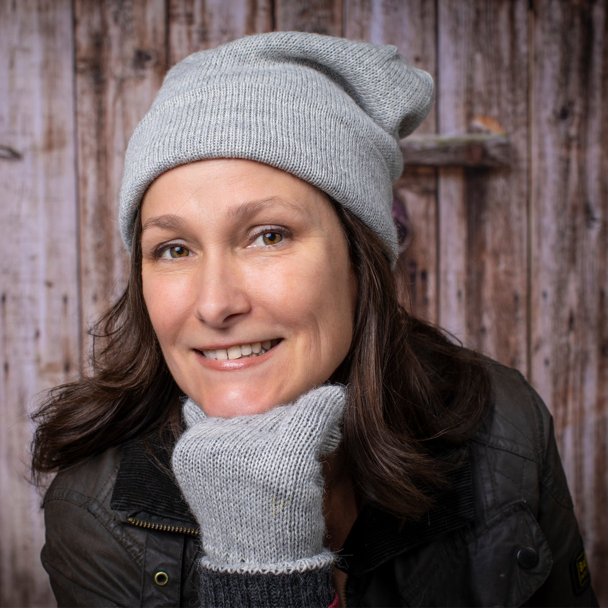 a smiling woman wears the silver iditarod hat and matching gloves posing casually with her chin resting on her gloved fist