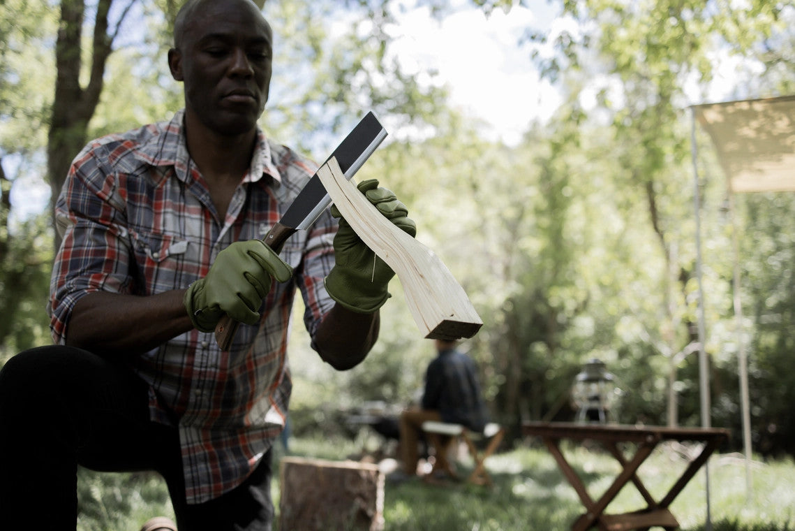 a man at a lush forest campsite splitting firewood with his japanese nata hatchet