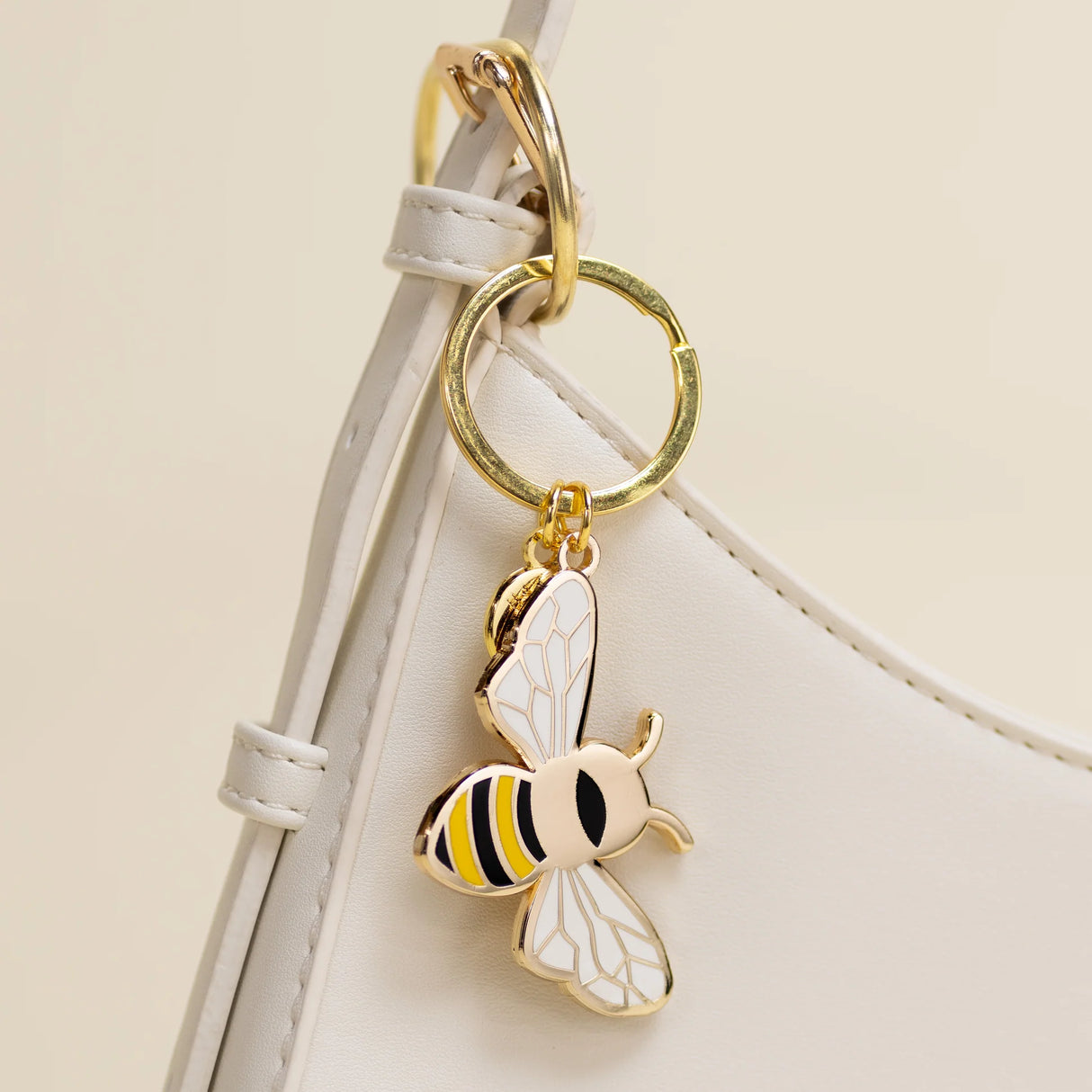 Gold bee-shaped keychain attached to a white strap on a beige background