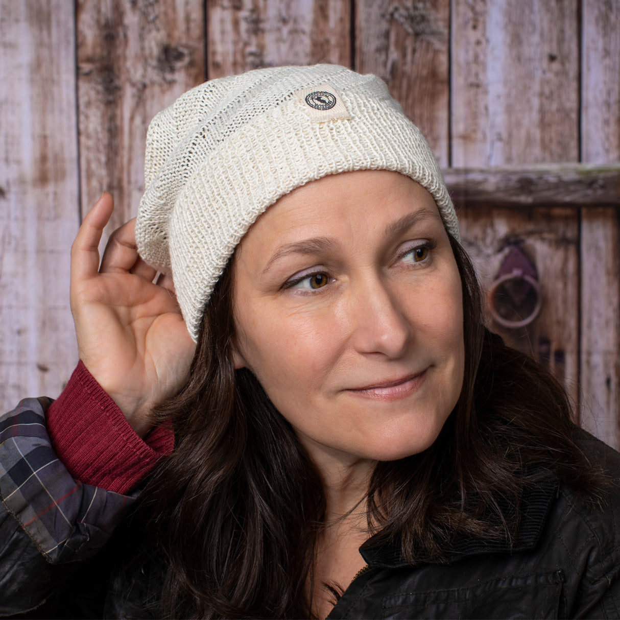 a fair skinned, brunette female model wearing the Cream beanie with her hand at the back of her head as if adjusting or styling it