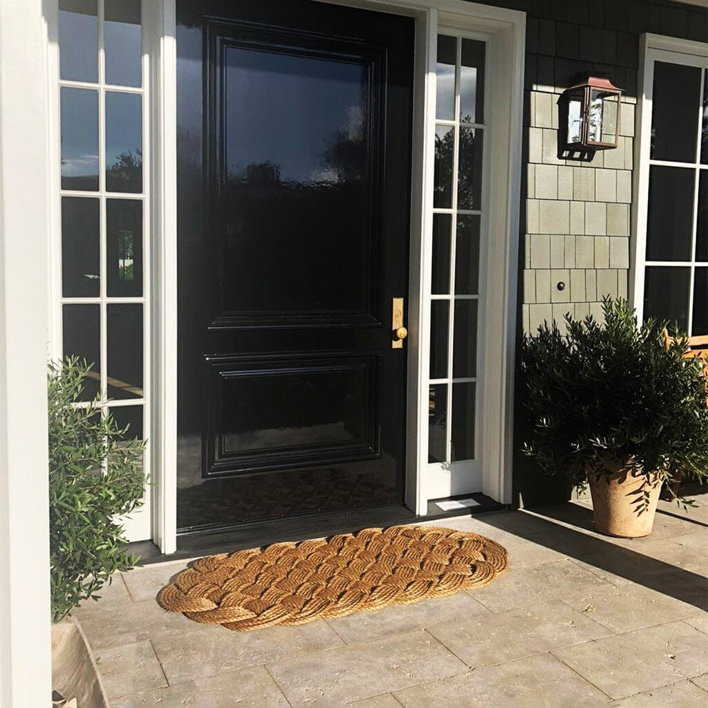 wide shot of a a large manila rope doormat with an intricate hand woven pattern on a doorstep in front of a navy blue door