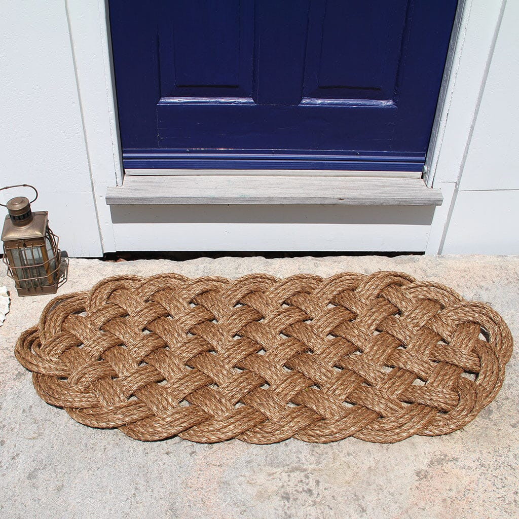 a large manila rope doormat with an intricate hand woven pattern on a doorstep in front of a navy blue door