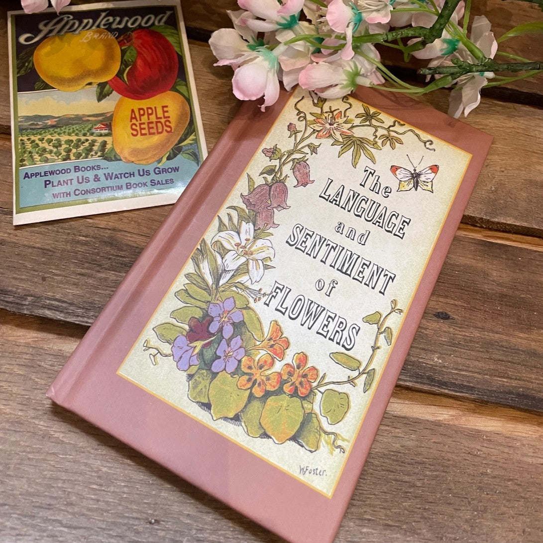 Book titled 'The Language and Sentiment of Flowers' on a wooden surface with a vintage Applewood Brand seed packet.