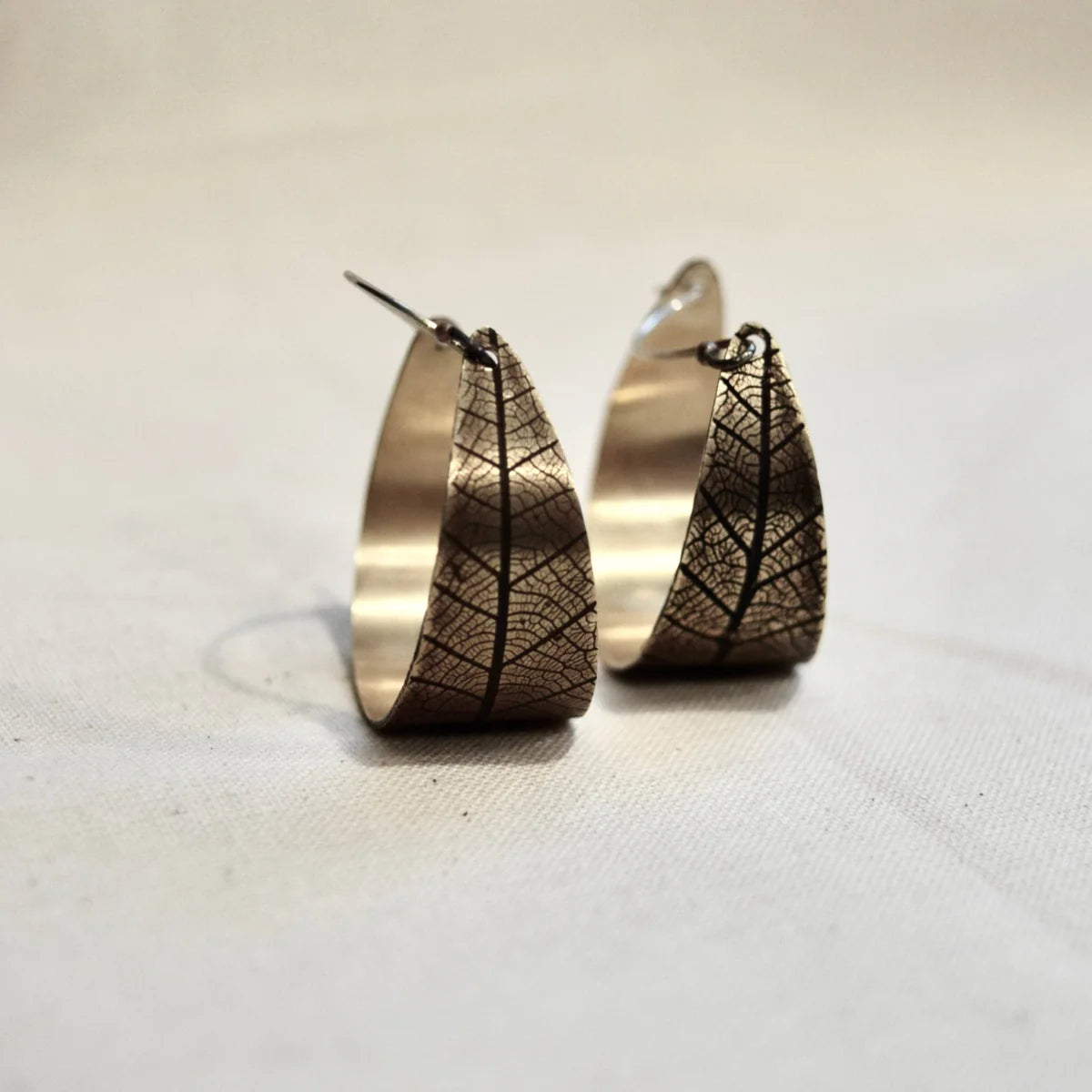 Pair of bronze hoop earrings with leaf-like patterns on a light background