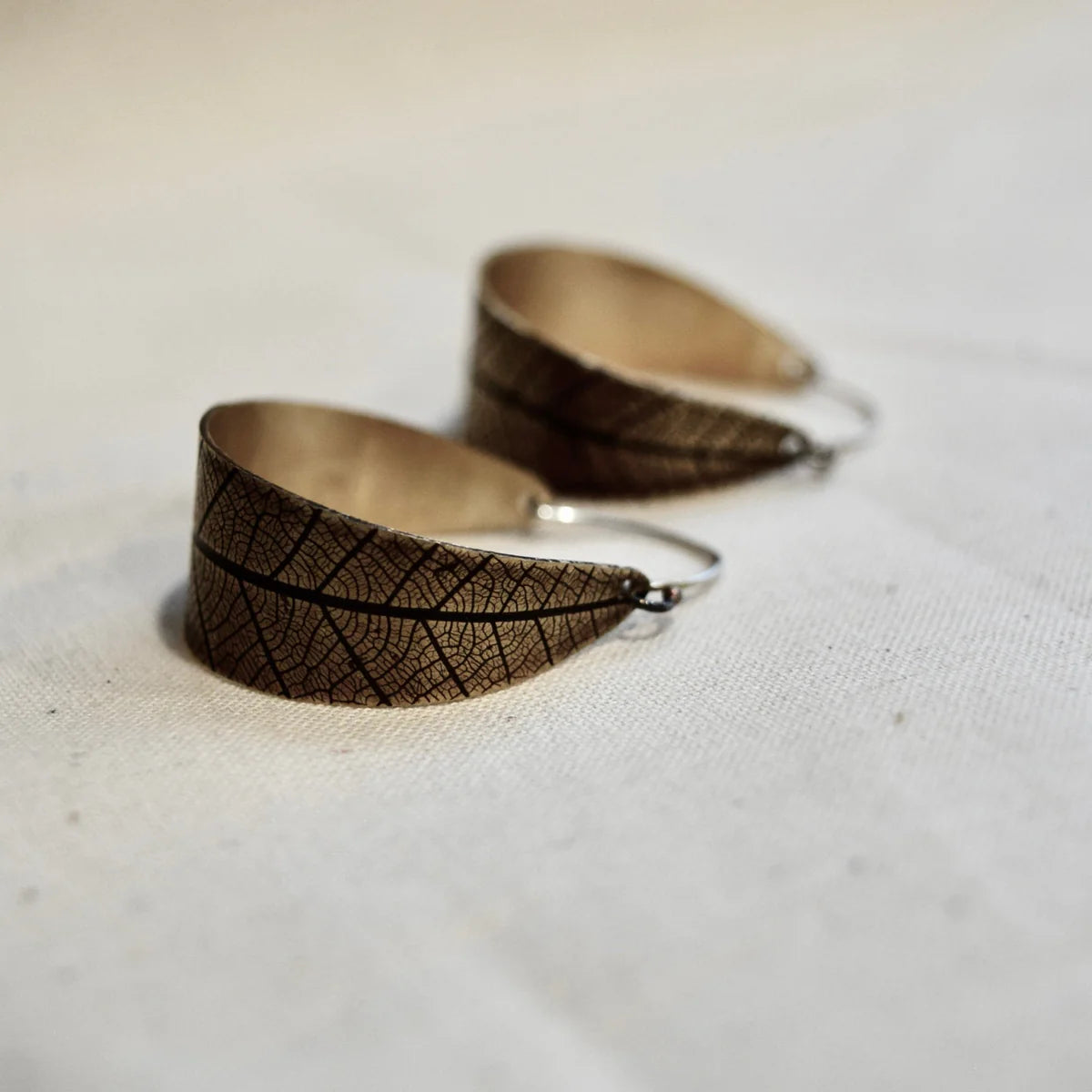 Pair of leaf-patterned earrings on a light fabric background