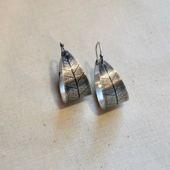 Silver leaf-shaped earrings on a beige fabric background