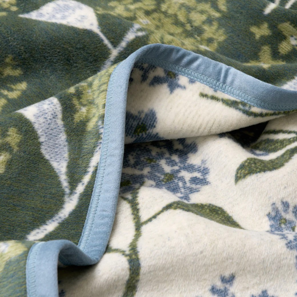 Close-up of a floral-patterned lilacs blanket with green, white, and blue colors.