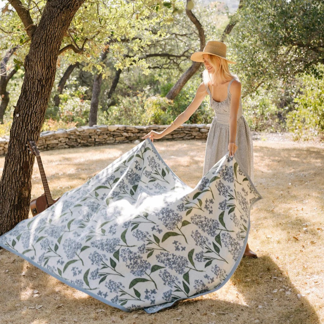 Woman setting up a floral-patterned picnic blanket outdoors.