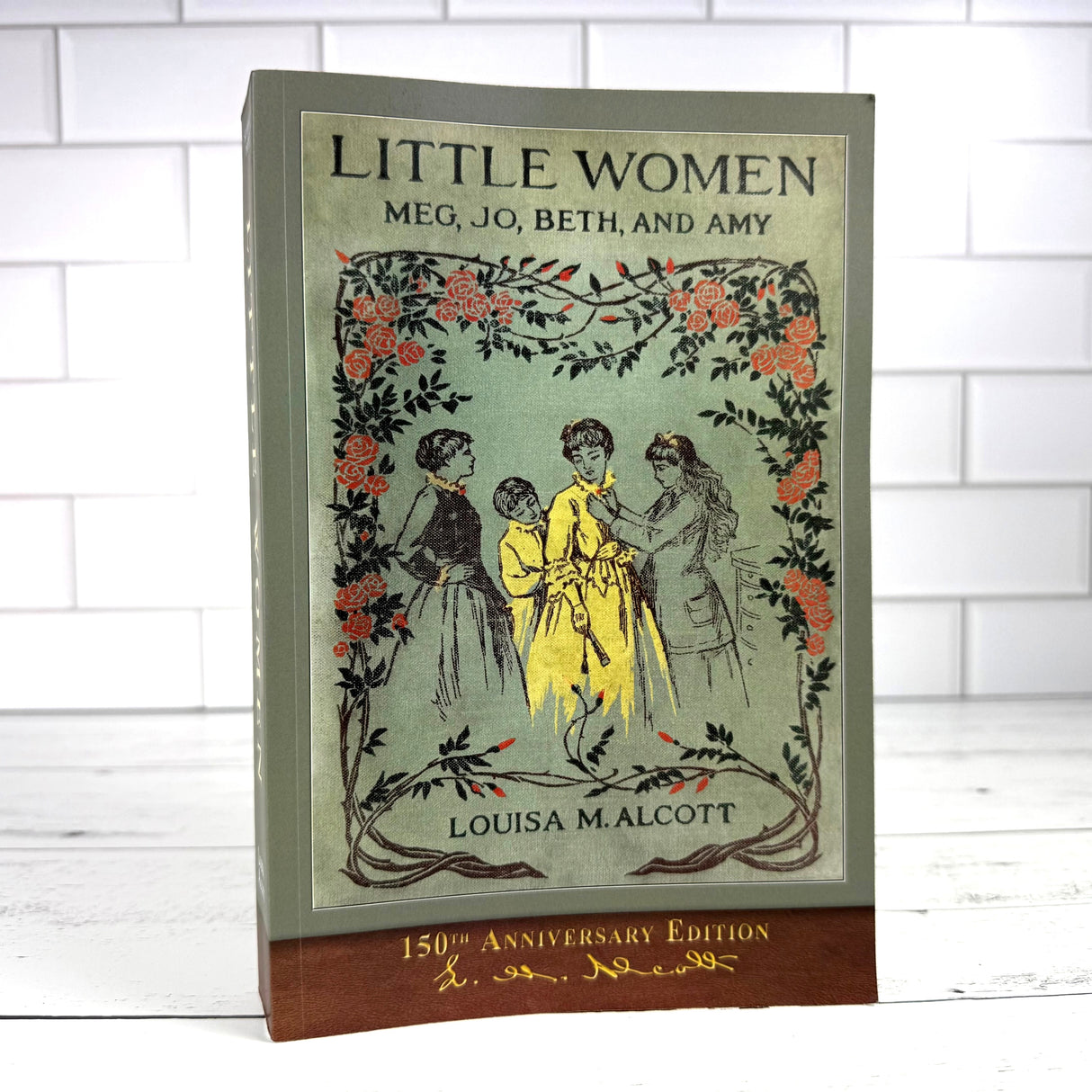 Little Women book standing on a white wood surface with a white tile background