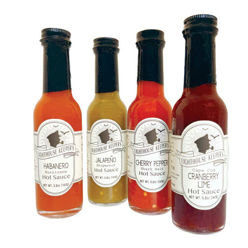 four slender bottles of hot sauce in vibrant hues from deep cranberry red to pea green to hot orange grouped together against a white background