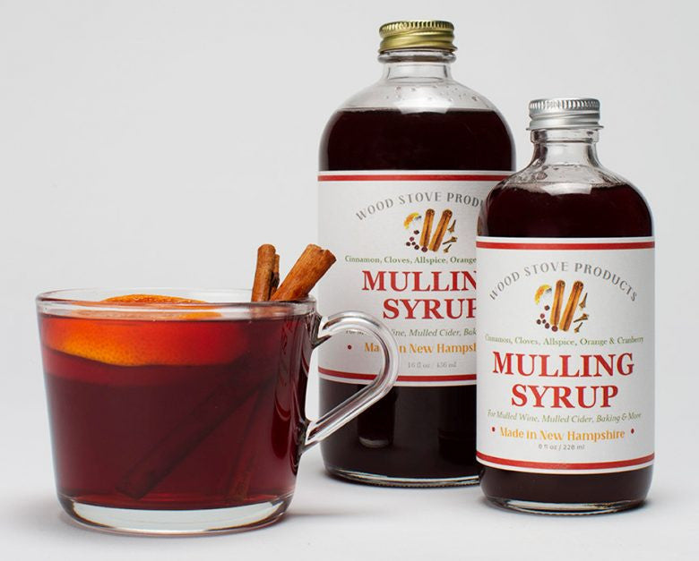 two bottles of mulling syrup next to a clear glass mug filled with a mulled beverage and two cinnamon sticks