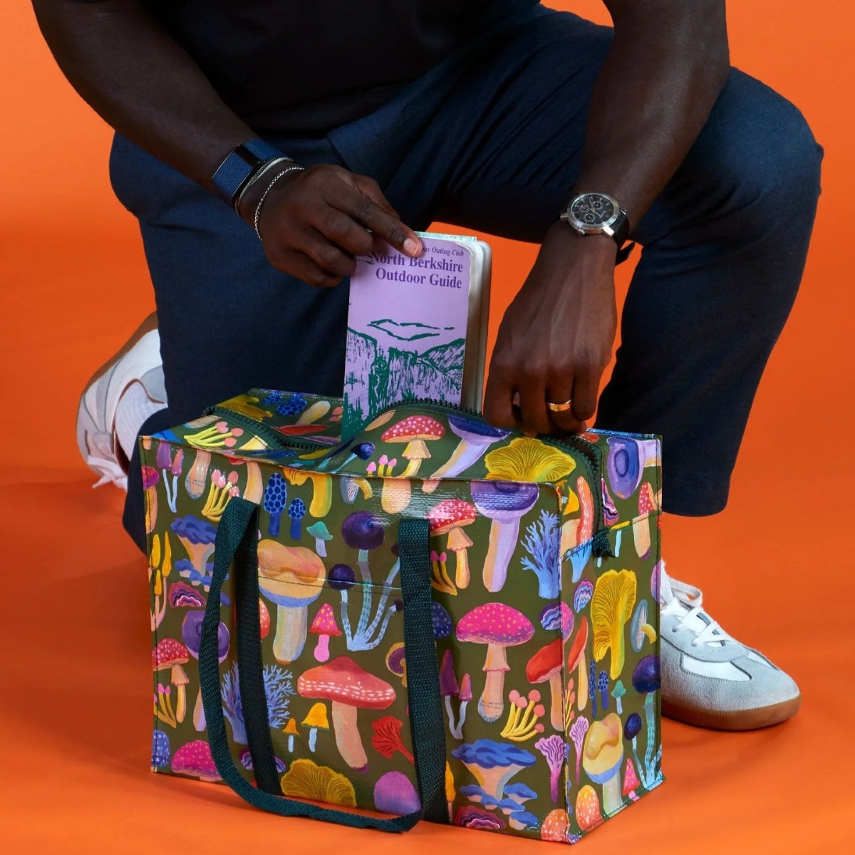 Person holding a colorful mushroom-patterned bag against an orange background
