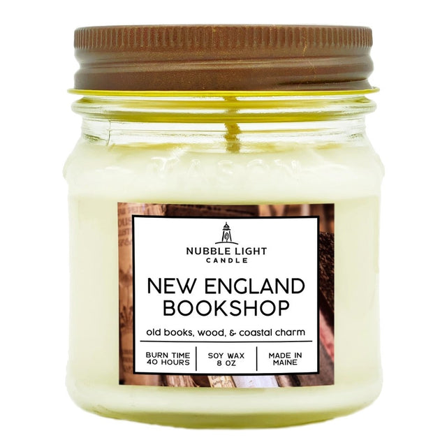 a candle in a clear glass mason jar with off white wax and a label that reads "New England Bookshop" against a white background