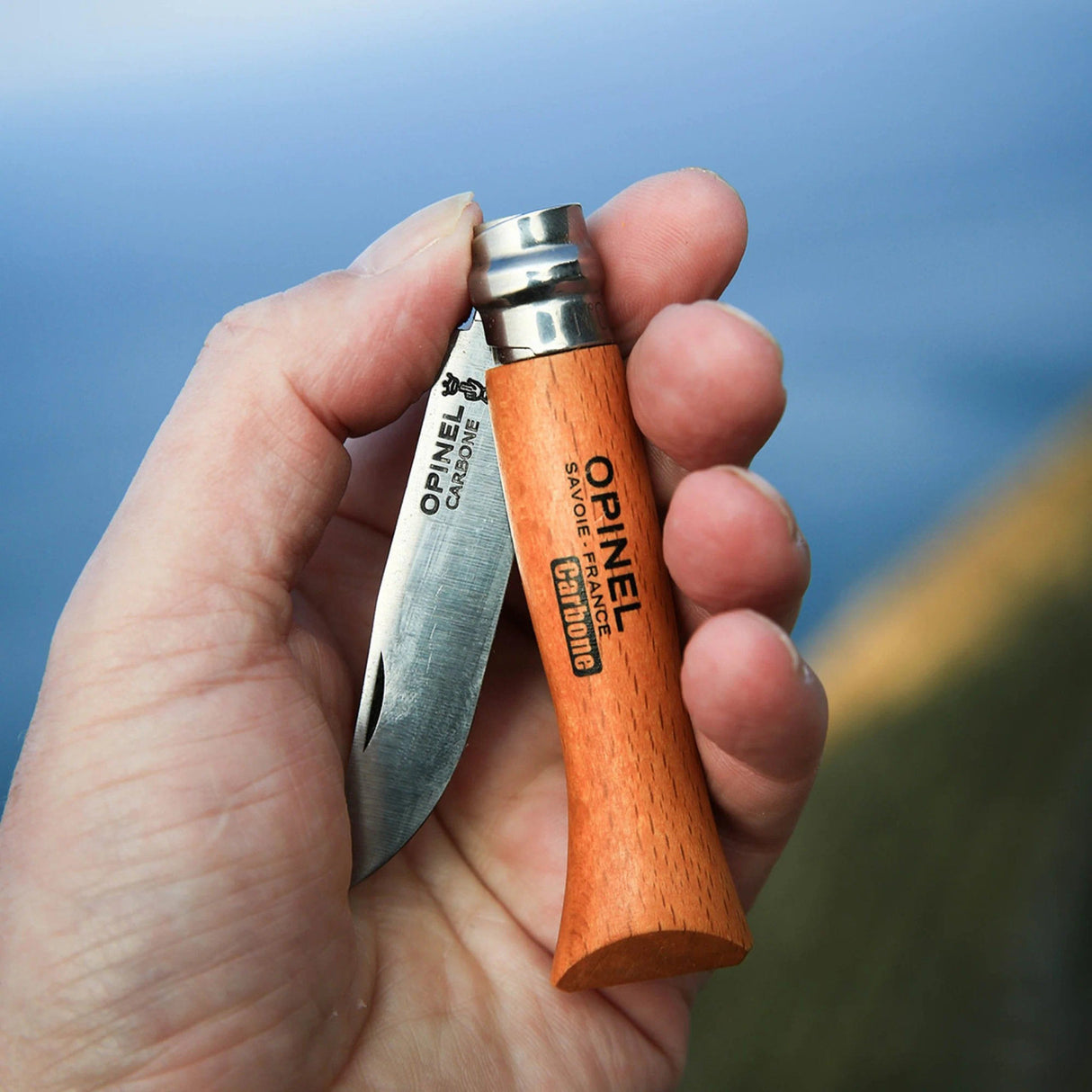 the Opinel Carbon steel folding knife held in someone's hand shown partially unfolded to show the scale of the knife handle