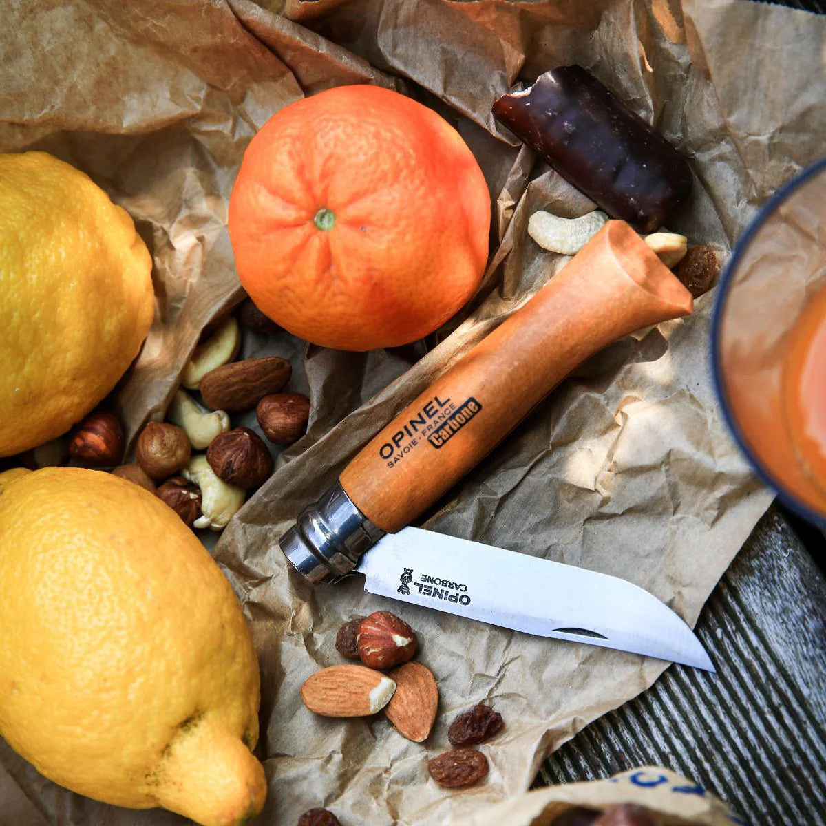 the carbon steel folding knife lying half unfolded amongst some snacks including nuts and citrus