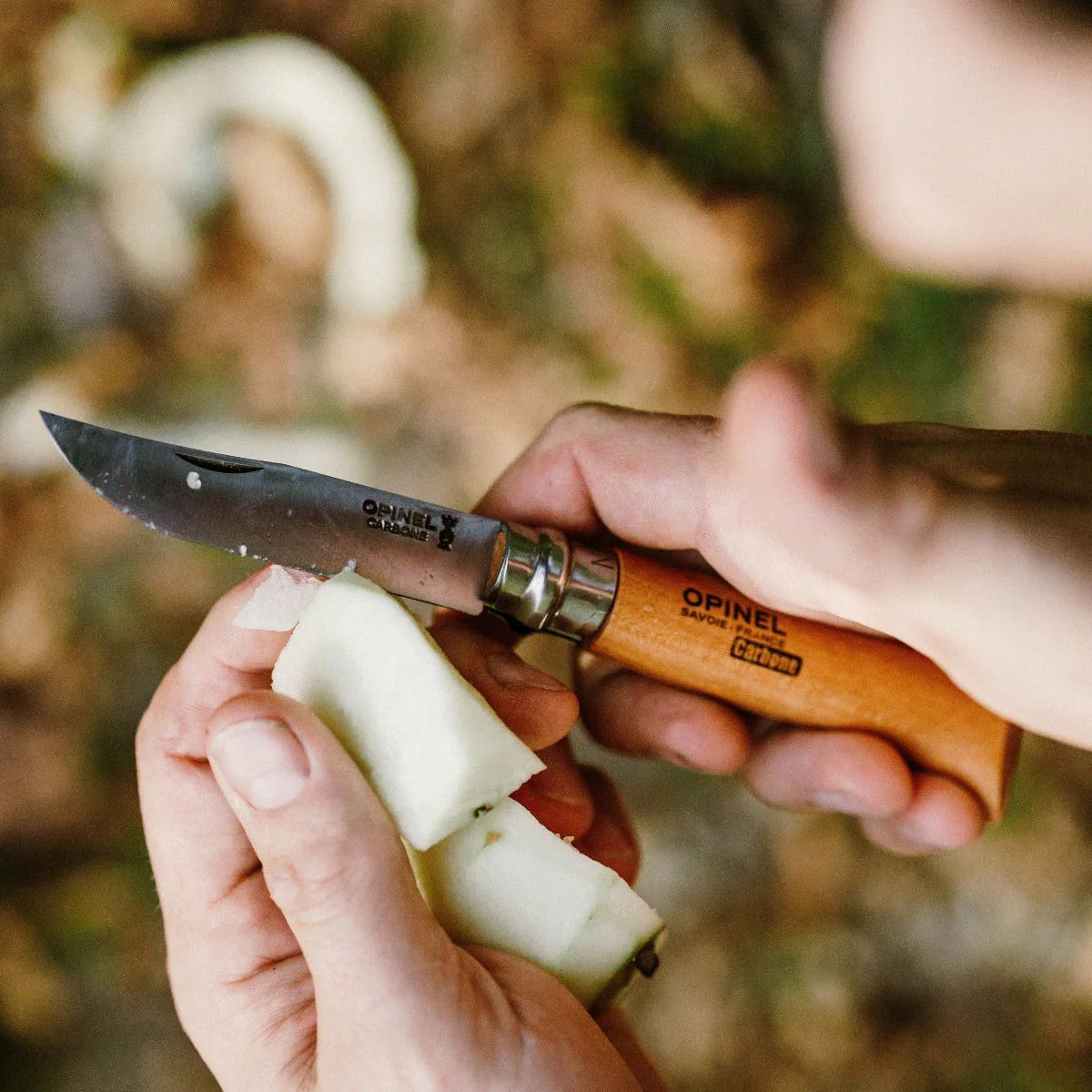 close up of two hands folding knife in one hand, apple in the other, as it is being sliced