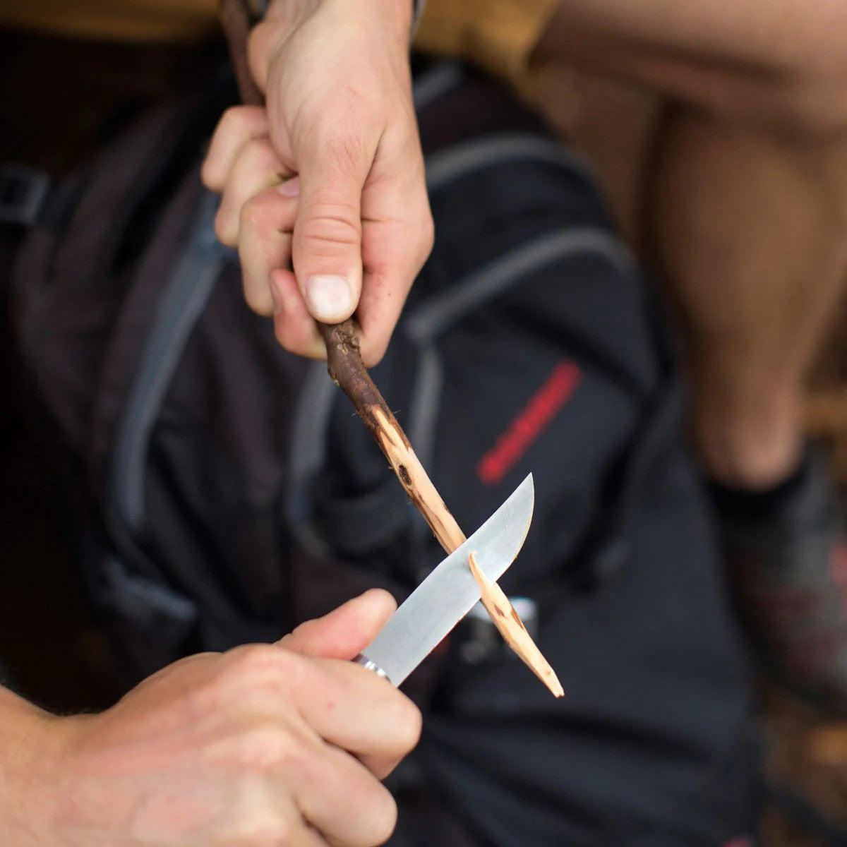 close up of two hands holding a small stick that is being carved by the folding knife