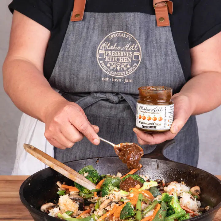 Person cooking with a jar of Blake Hill Preserves in a kitchen setting