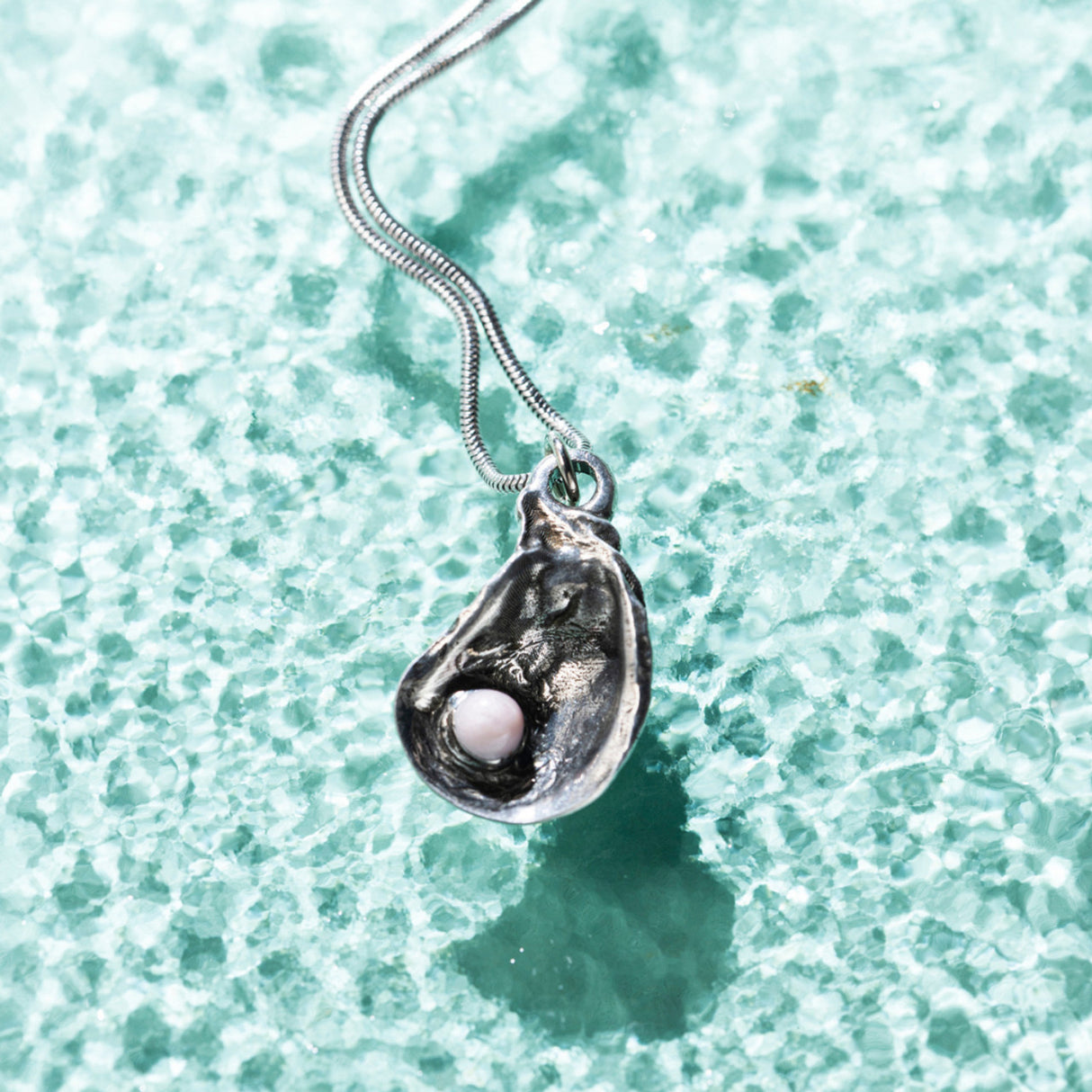 Silver Oyster Shell Necklace with a pendant molded from a real oyster shell, featuring delicate pink pearl-like decorations against a sea green background with water-like texture