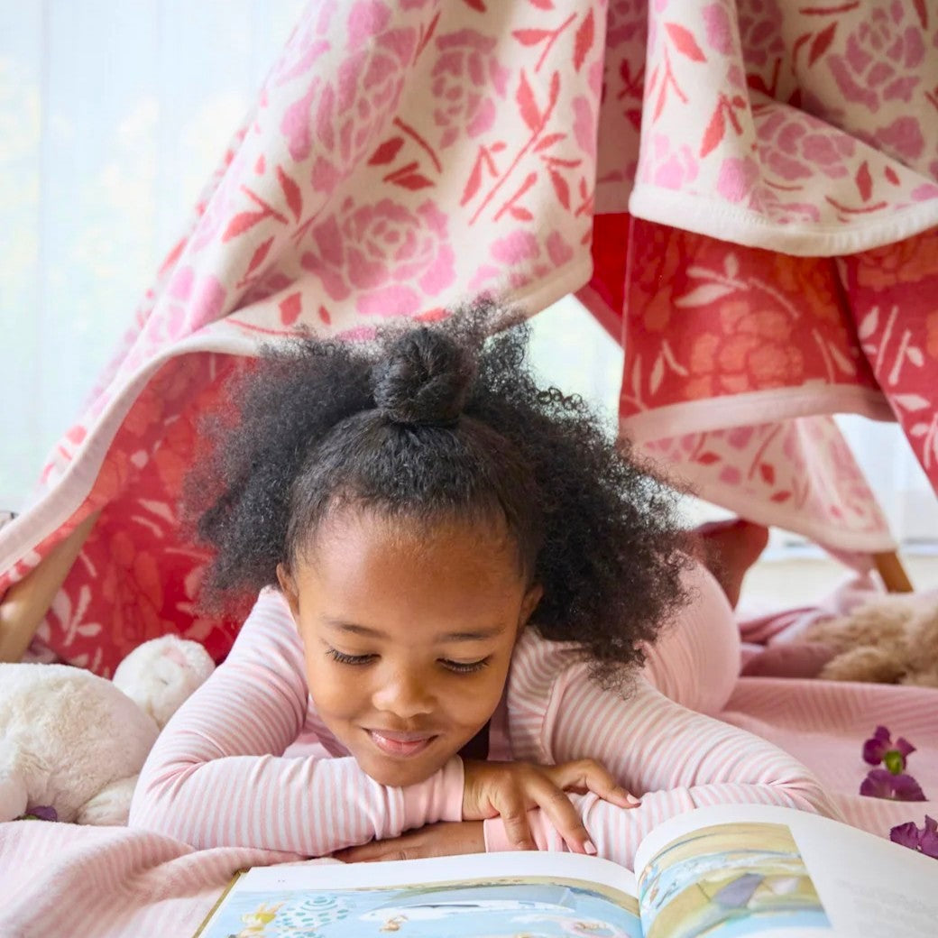 Child reading a book under a floral blanket