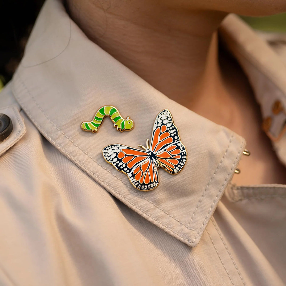 Butterfly and caterpillar-shaped pins on a beige jacket lapel