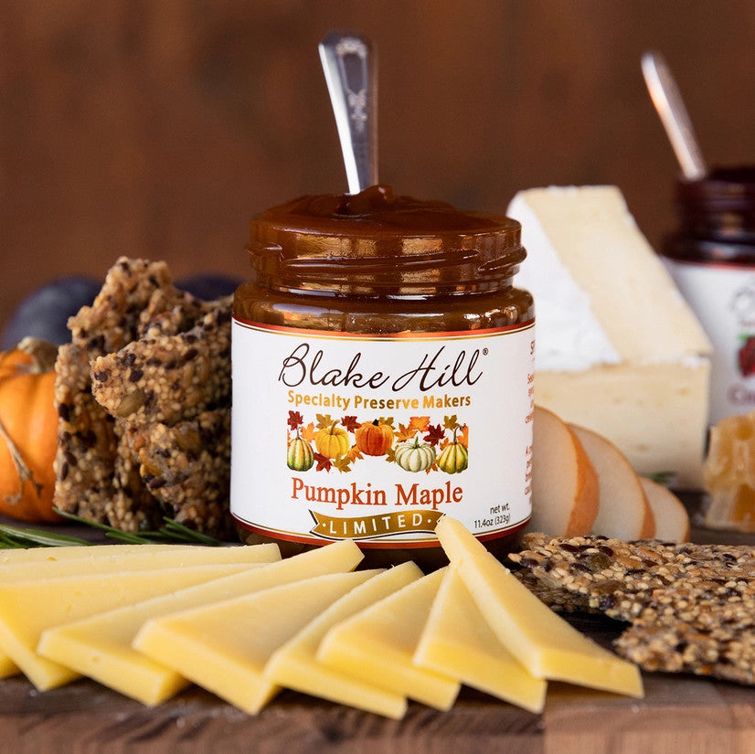 a board with fanned cheeses and crackers and a jar of pumpkin maple butter with a spoon in it