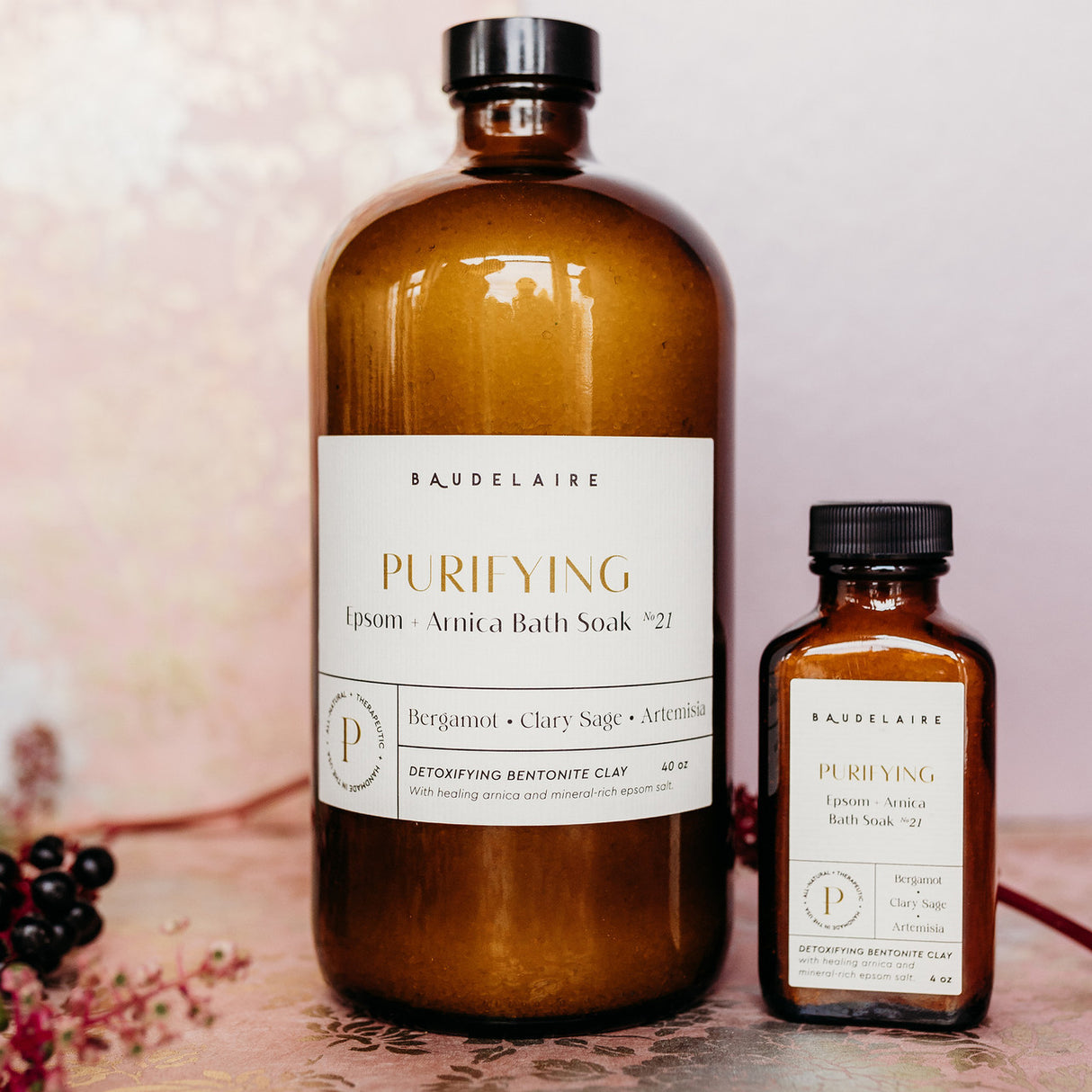 a large 40 ounce bottle of the Epsom + Arnica soak alongside a small 4 ounce bottle of the spring blossom soak on a table surrounded by flower petals