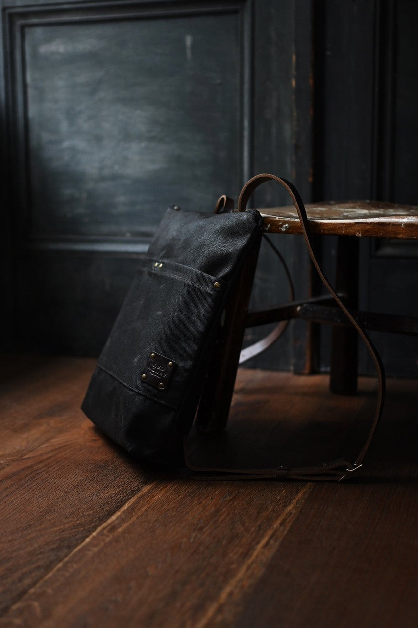 the Day Pack in Chocolate rests against a chair in a dark rustic room