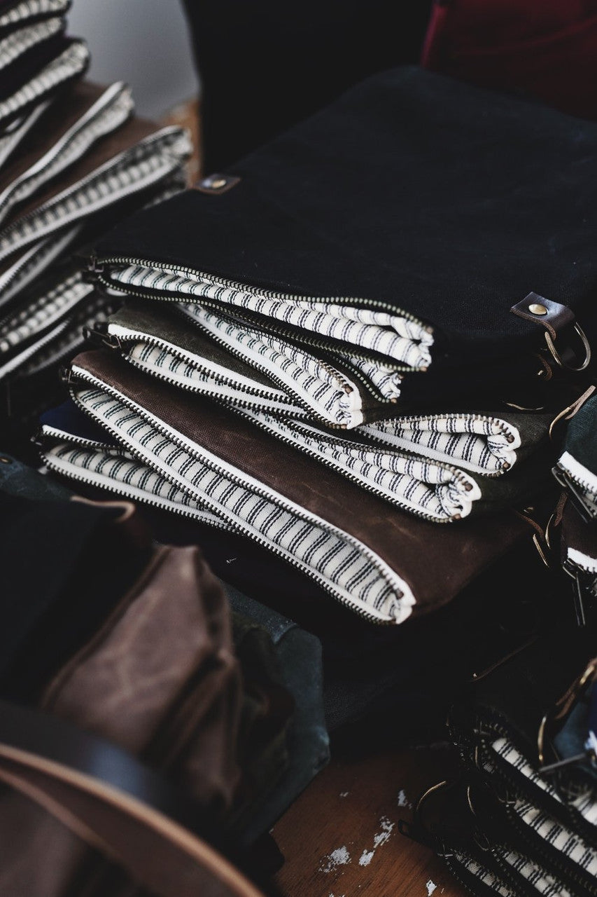 a stack of various colored day packs in a stack, unzipped, showing the light striped bag interior