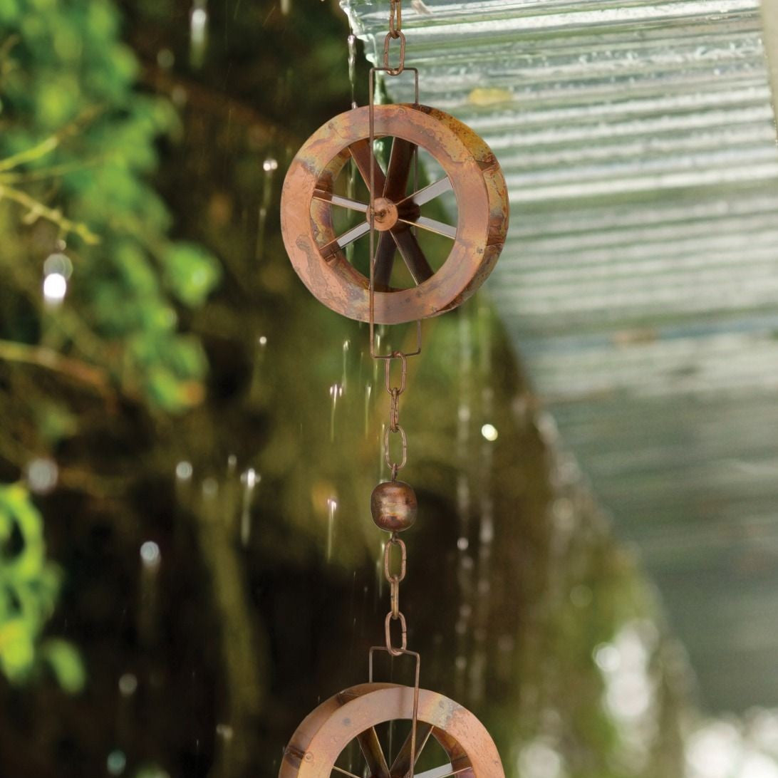a close up of two of the water wheels from the rain chain with a rainy garden in the background
