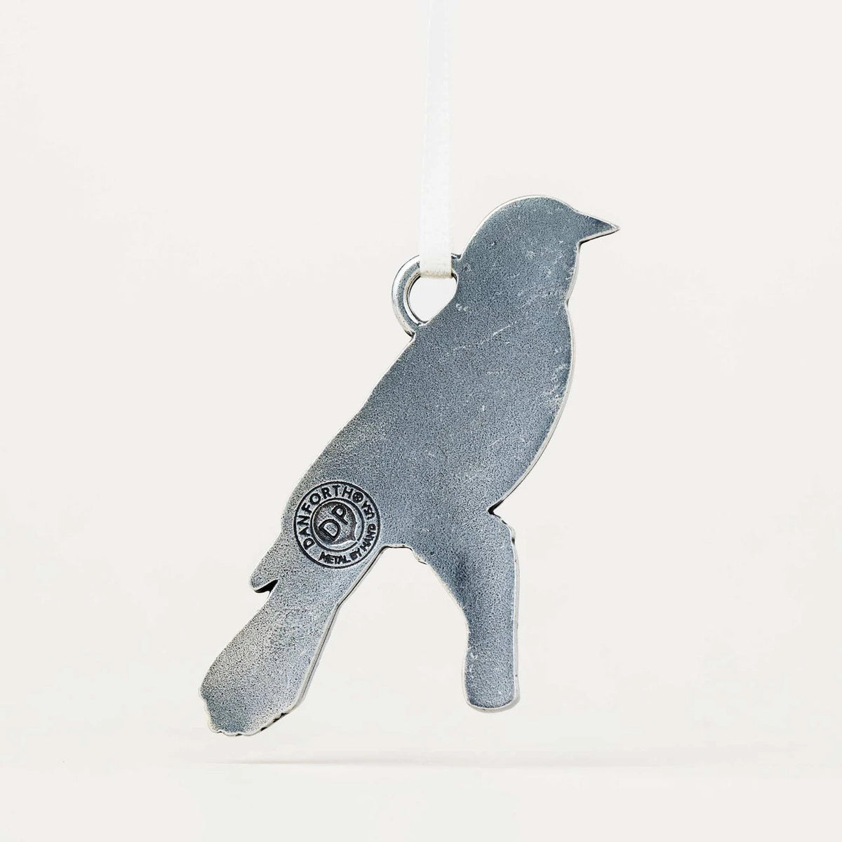 A silver bird-shaped hanging ornament with a textured finish, featuring a circular brand stamp on its side and a white hanging ribbon at the top, shown against a plain off-white background.