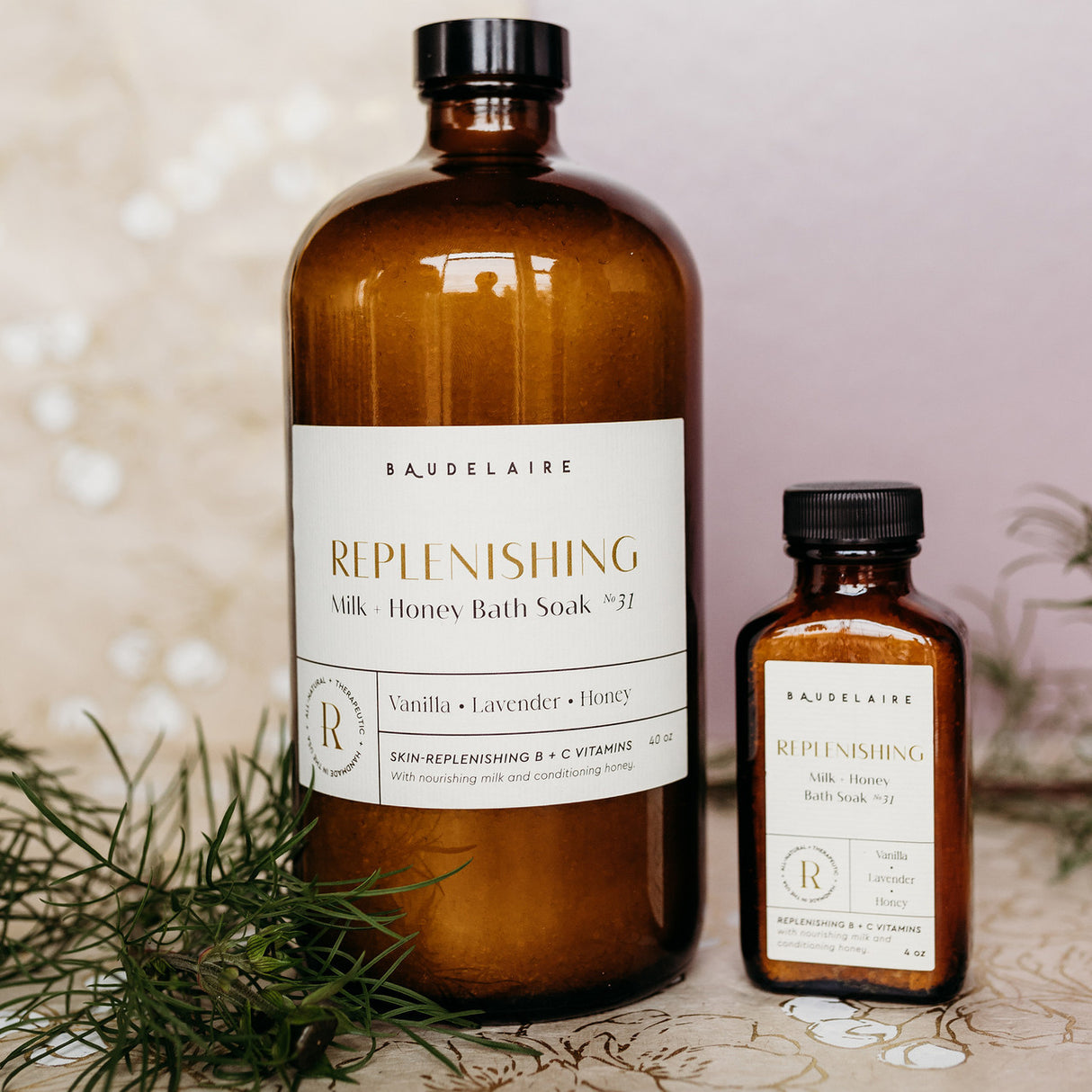 a large 40 ounce bottle of the Milk + Honey soak alongside a small 4 ounce bottle of the spring blossom soak on a table surrounded by flower petals