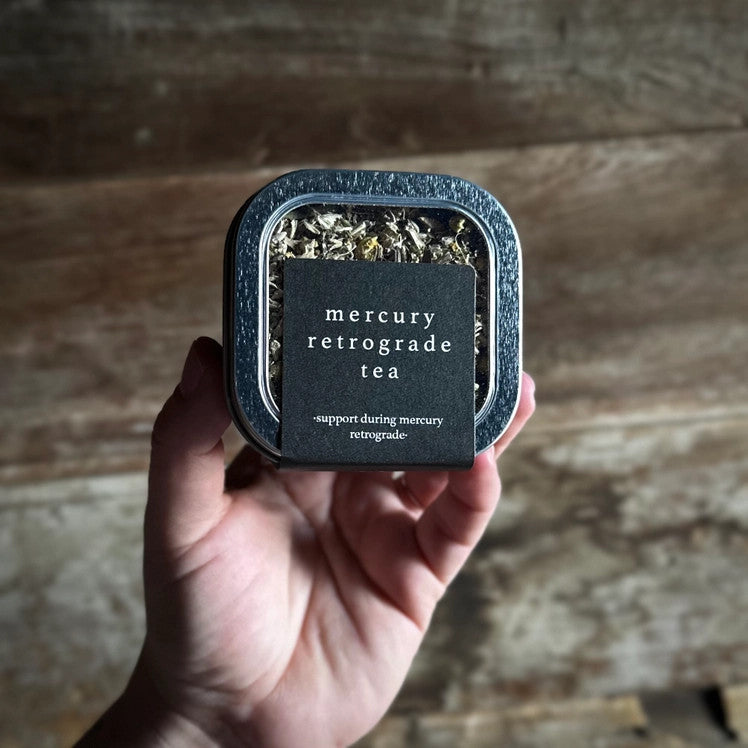 a wide view of a hand holding the mercury retrograde tea tin