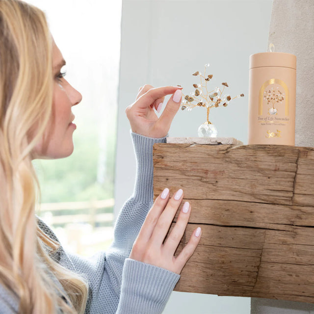 A model adjusting the branches of her tree of life suncatcher on a rustic wood mantle