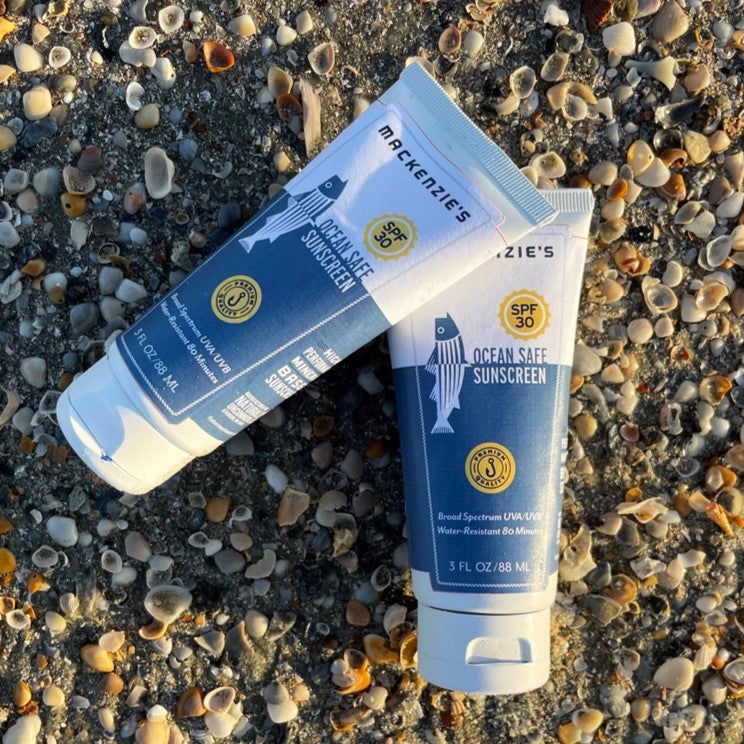 2 blue and white sunscreen bottles on a rocky beach