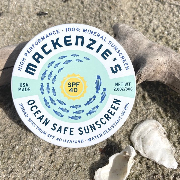 a round tin of ocean safe sunscreen on a sandy beach with shells