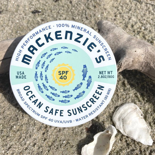 a round tin of ocean safe sunscreen on a sandy beach with shells