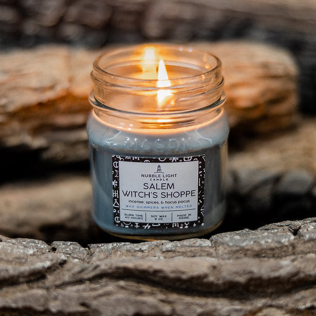 Candle in a mason jar labeled 'Salem Witch's Shoppe on a stone surface