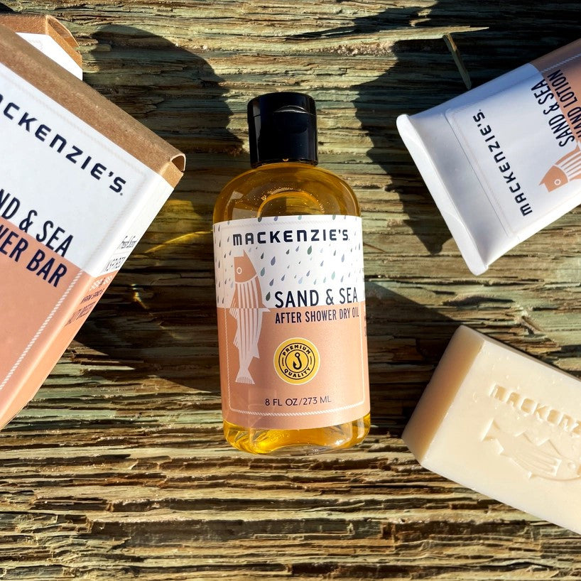 the Sand and Sea Sampler products spread on a wooden dock with the Sand and Sea After Shower Dry Oil in the center
