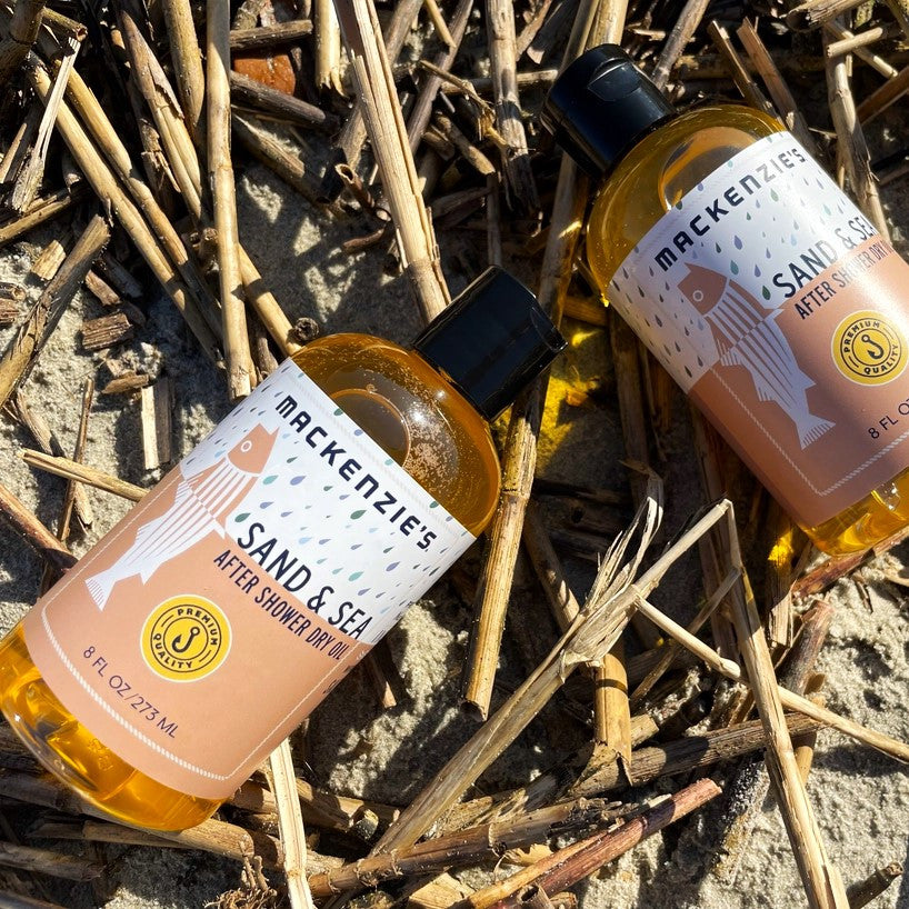 Two bottles of the Sand and Sea After Shower Dry Oil on a sandy beach