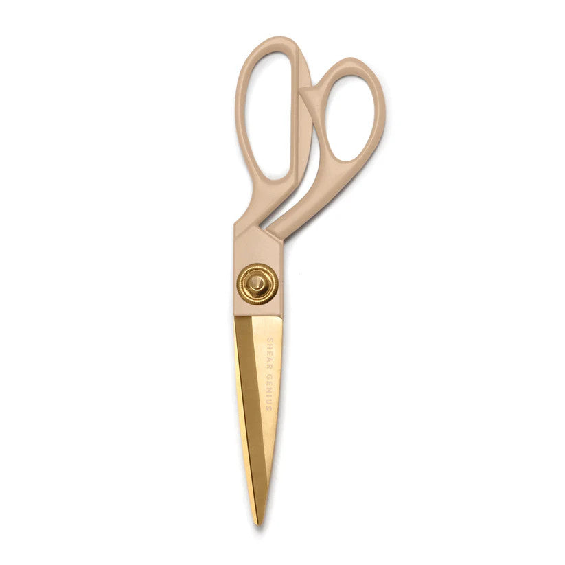 a vintage inspired pair of scissors with taupe enamel handles and gold blades etched with the phrase "Shear Genius" against a white background
