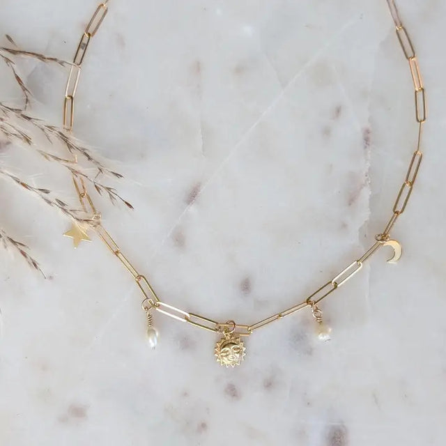 a gold paperclip chain with 14k gold fill charms of the sun, moon, and stars paired with delicate freshwater pearls